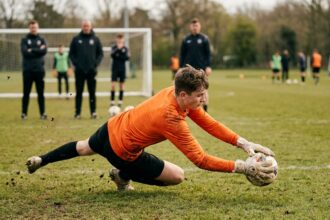 Jeune gardien de but plongeant pour arrêter un ballon lors d'un stage d'entraînement sur terrain en herbe