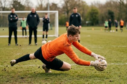 Jeune gardien de but plongeant pour arrêter un ballon lors d'un stage d'entraînement sur terrain en herbe